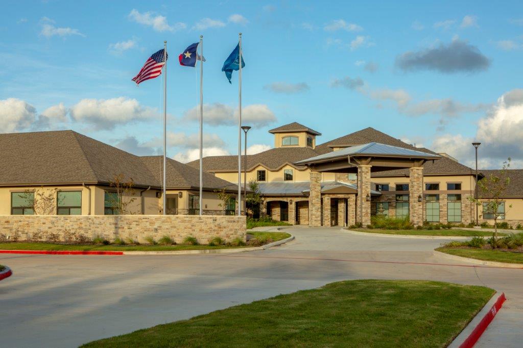 The Shores at Clear Lake main beige building with dark brown roof, and three flags in front of the building.