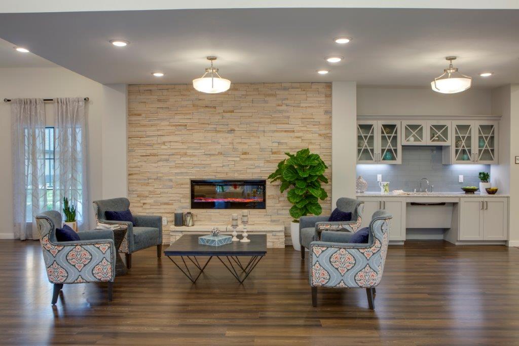 A sitting room with a digital fireplace, square brown coffee table, and light blue sofa chairs around it at The Shores at Clear Lake.