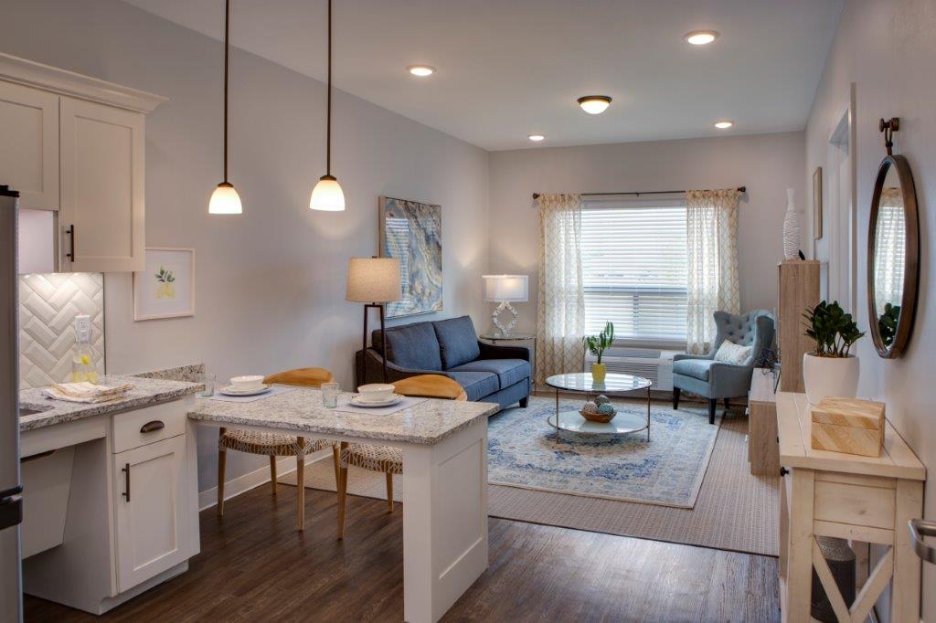 A living room that's connected to the living room with a round coffee table in the middle of the room with a potted plant on it, a blue couch to the left, and a light blue sofa chair to the right at The Shores at Clear Lake.