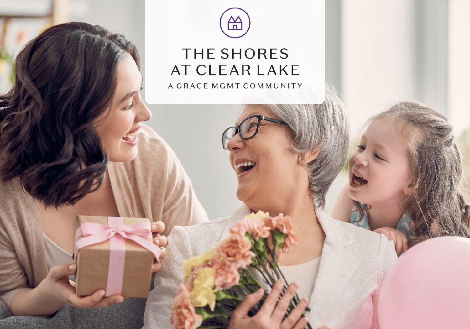 Smiling young woman gives a gift to an elderly woman holding flowers; a little girl laughs beside them at The Shores at Clear Lake.
